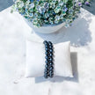 Black beaded bracelet on white pillow, ideal for protection and spiritual growth, with floral backdrop