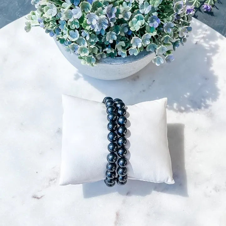 Black beaded bracelet on white pillow, ideal for protection and spiritual growth, with floral backdrop