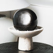 Polished black crystal sphere on textured stone pedestal, ideal for healing and spiritual decor