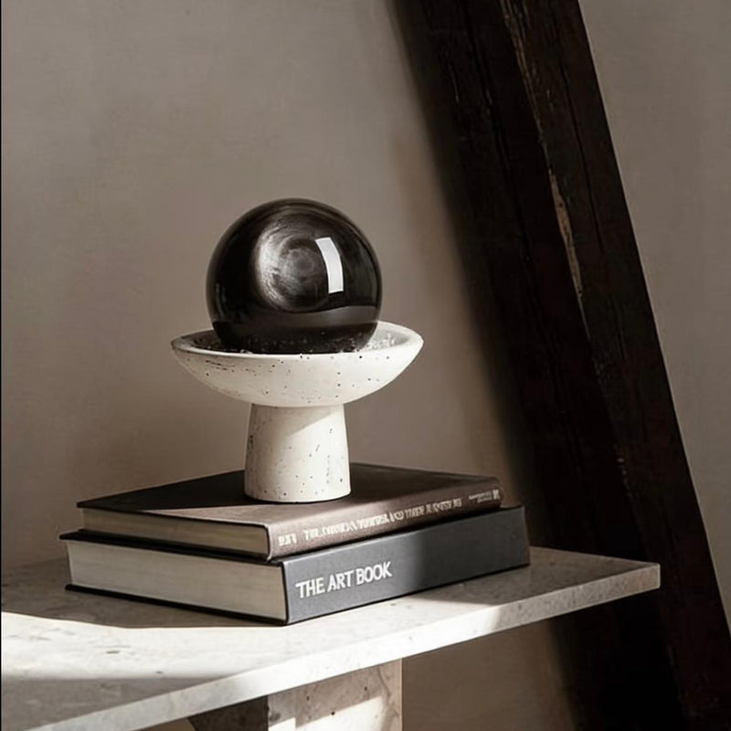 Black crystal sphere on speckled pedestal atop books, ideal for spiritual decor and chakra healing