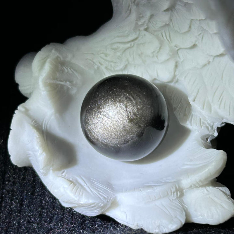 Shiny metallic sphere in white carved holder, healing crystal for spiritual growth and protection