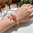 Hand wearing pink crystal paw charm bracelet with gold accents, perfect for love and spiritual healing.
