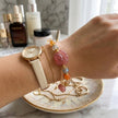 Hand wearing pink and orange gemstone bracelet with gold chain, paired with watch on marble vanity