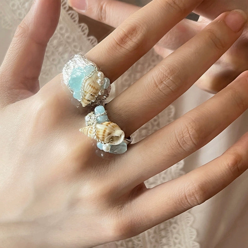 Hand wearing two seashell and aquamarine gemstone rings, boho beach jewelry for spiritual healing