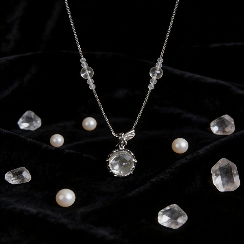 Clear quartz crystal necklace with angel pendant, surrounded by raw crystals and pearls on black velvet
