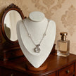 Clear quartz crystal necklace with silver chain, displayed on mannequin with vintage mirror and perfume bottle