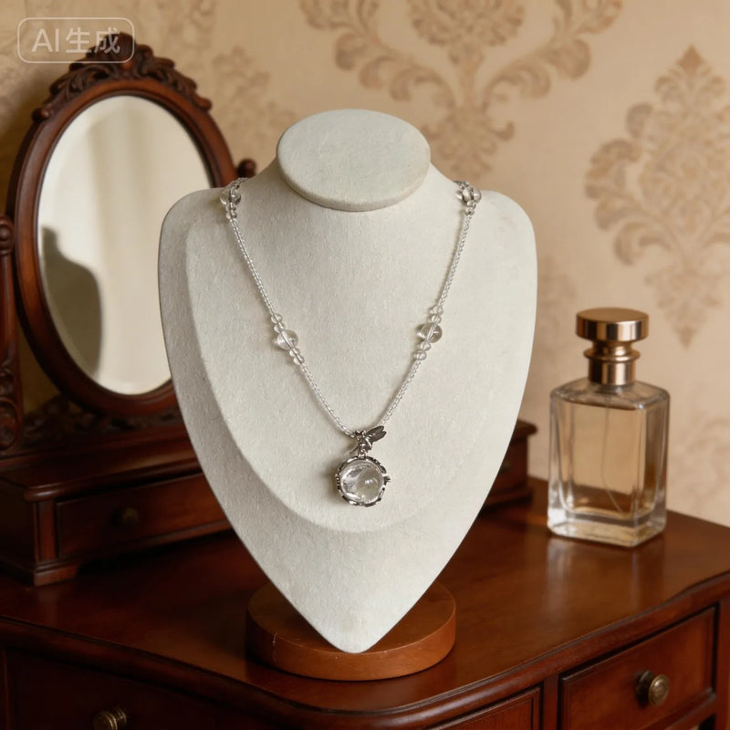 Clear quartz crystal necklace with silver chain, displayed on mannequin with vintage mirror and perfume bottle