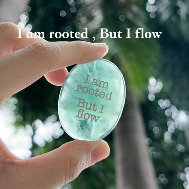 Hand holding engraved aquamarine crystal with 'I am rooted, But I flow' for spiritual growth and calm