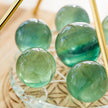 Smooth green crystal spheres for chakra healing and spiritual growth, displayed on a glass stand.