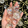 Hand holding clear rainbow aura quartz spheres on black gold constellation cloth for spiritual healing and chakra balance
