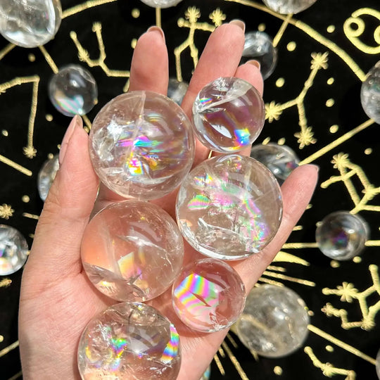 Hand holding clear rainbow aura quartz spheres on black gold constellation cloth for spiritual healing and chakra balance