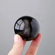 Hand holding a polished black obsidian sphere for protection and spiritual healing