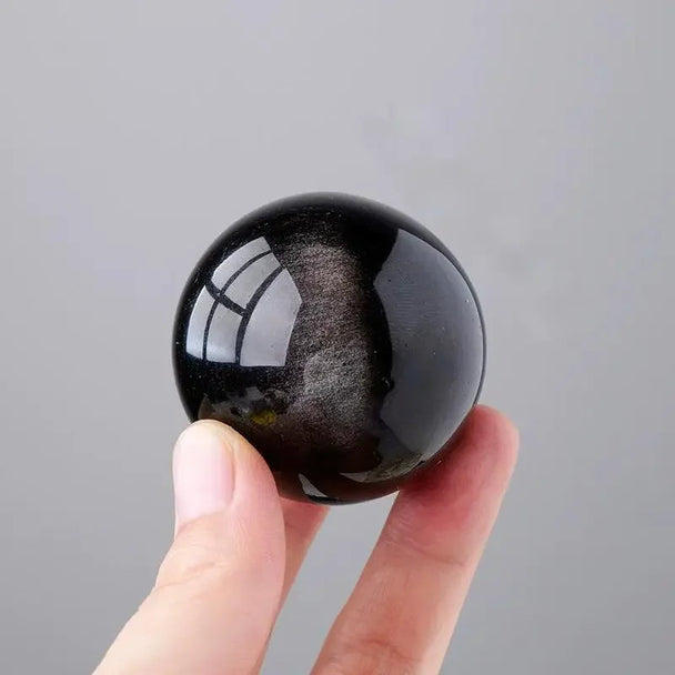 Hand holding a polished black obsidian sphere for protection and spiritual healing
