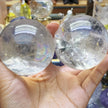 Hand holding two clear quartz crystal spheres with natural inclusions, ideal for healing and spiritual practices.