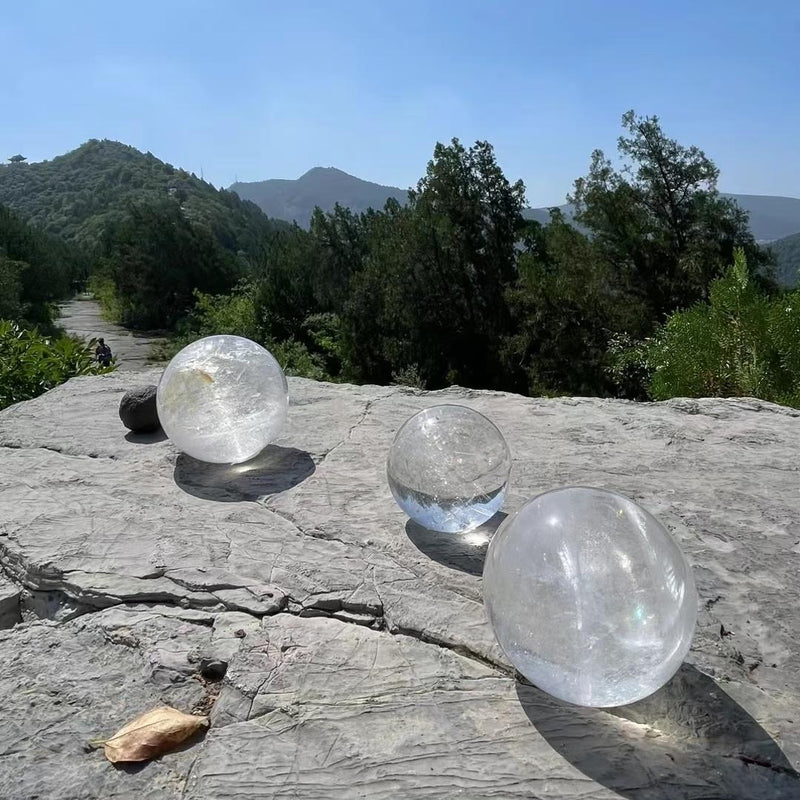 Clear quartz crystal spheres on rocky ledge with mountain view, ideal for spiritual healing and energy work