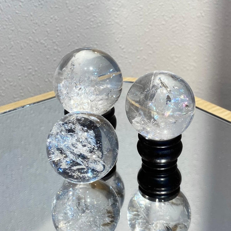 Clear quartz crystal spheres with inclusions, displayed on black stands for spiritual healing and energy work