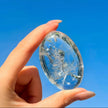 Clear quartz crystal egg with etched design, held against blue sky for spiritual healing and energy work