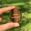 Tiger eye crystal with 'Solvitur ambulando' engraving, held outdoors for grounding and spiritual growth.