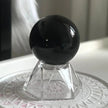Polished black obsidian sphere on crystal stand for protection and spiritual healing