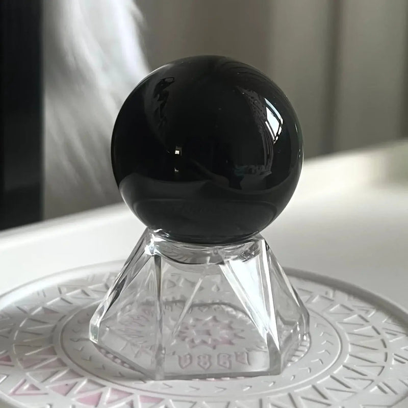 Polished black obsidian sphere on crystal stand for protection and spiritual healing