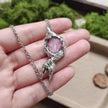 Handmade pink crystal pendant necklace with textured silver setting, held in hand against green moss background