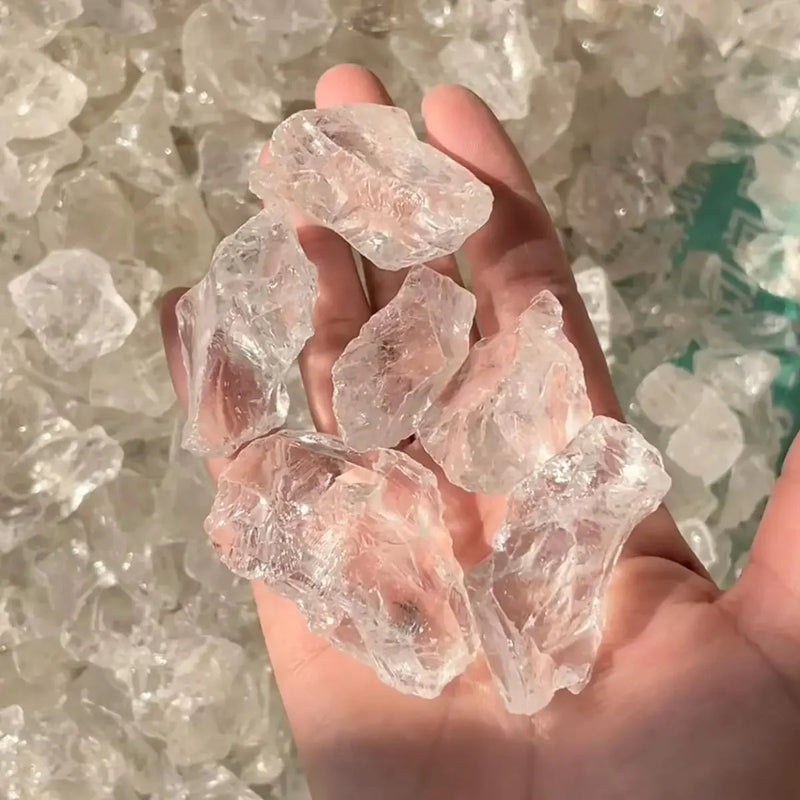Hand holding clear quartz crystals for healing and spiritual growth, surrounded by raw gemstones.