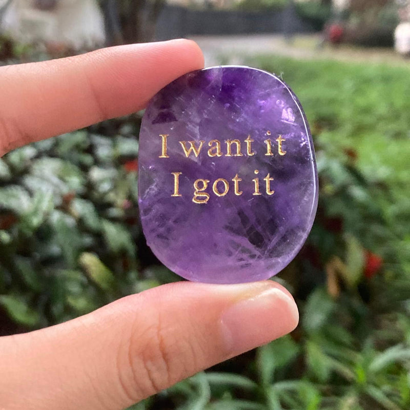 Amethyst crystal stone with gold 'I want it I got it' engraving, held in hand outdoors