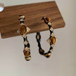 Tiger eye gemstone hoop earrings with gold accents and crystal details, displayed on wood