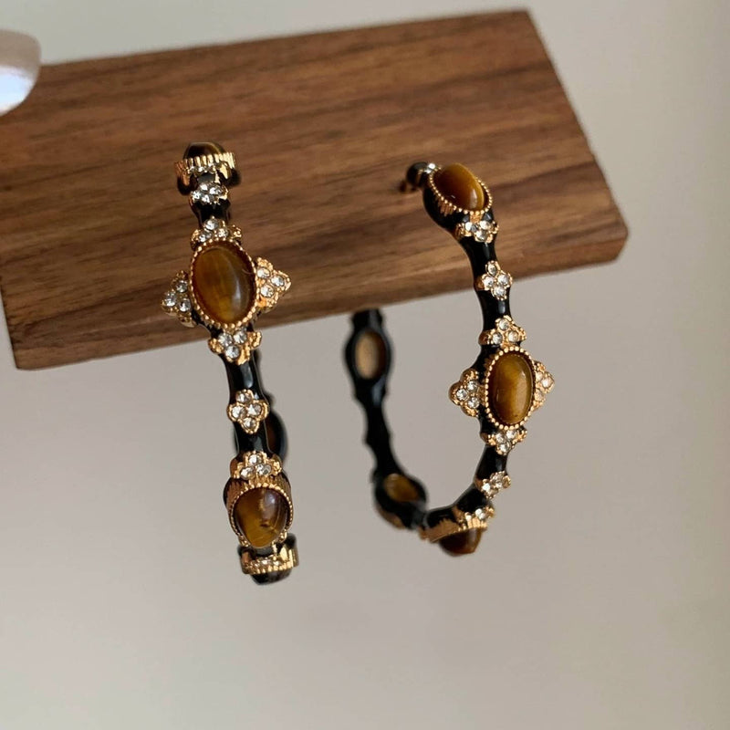 Tiger eye gemstone hoop earrings with gold accents and crystal details, displayed on wood