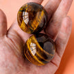 Two polished tiger eye crystal spheres held in hand, ideal for chakra healing and spiritual growth.