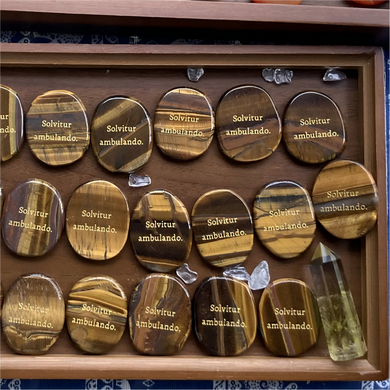 Tiger eye stones engraved with 'Solvitur ambulando,' displayed in wooden tray with clear crystals