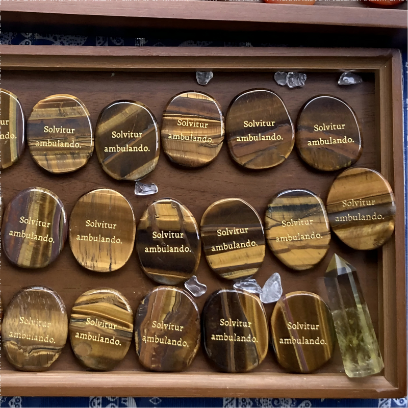 Tiger eye stones engraved with 'Solvitur ambulando' in wooden display, healing crystals for spiritual growth