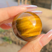 Hand holding polished tiger eye crystal sphere for protection and spiritual growth