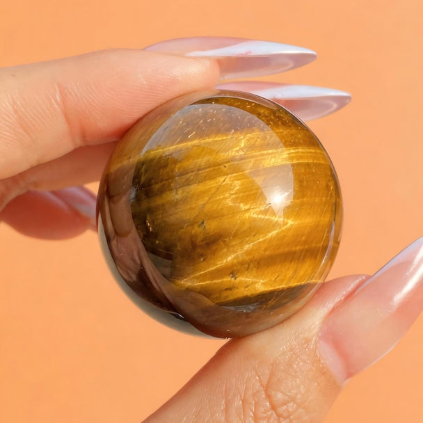 Hand holding polished tiger eye crystal sphere for protection and spiritual growth